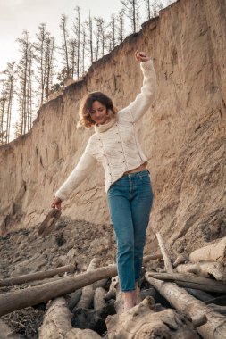 Doğal yün ve kottan yapılmış kahverengi örgü kazak giymiş genç moda kadın Moda yaşam tarzı portre gülerek, gülümseyerek, plaj poz; ağaçlar ile arka planda kumlu yamaç. Neşeli kadın portresi