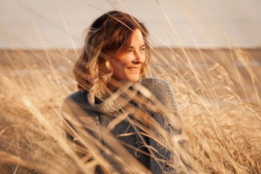 Örgü şapka ve sıcak giysiler güzel bir genç model portresi güneşli sonbahar gününde arka plan alanında, gün keyfini çıkarın. Kadın ve doğanın birliği kavramı, huzurlu ruh hali, çevre dostu yaşam