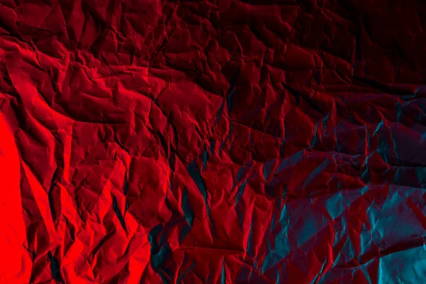 Texture of crumpled black paper. Close up black background of crumpled cardboard under red studio light