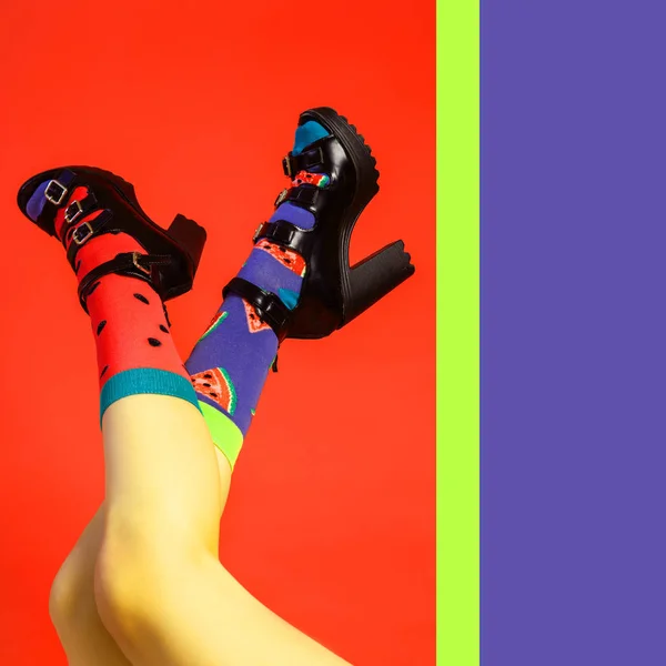 Concept of merry summer mood, relaxation and beauty. Female legs in black shoes with heels and bright color socks with a watermelon print and seeds on an isolated bright pink, yellow, blue background