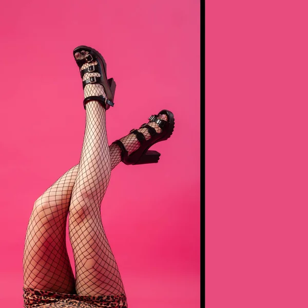 Concept of merry summer mood, relaxation and beauty. Female legs in black heels and black pantyhose in mesh on an isolated bright pink, yellow, green background