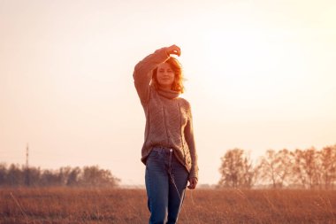 Kadın ve doğanın birliği kavramı, huzurlu ruh hali, çevre dostu yaşam. Kısa saç kesimi ve şık giysiler (örme kazak ve kot pantolon) ile genç kadın yürür ve bir yaz sabahı alanında doğanın tadını çıkarır