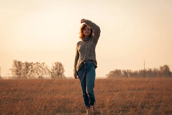 The concept of the unity of women and nature, peaceful mood, eco-friendly life.Young woman with a short haircut and in stylish clothes (knitted sweater and jeans) walks and enjoys nature in the field on a summer morning