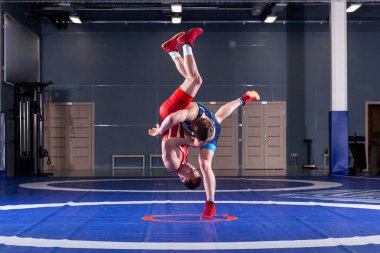 The concept of fair wrestling. Two greco-roman  wrestlers in red and blue uniform wrestling   on a wrestling carpet in the gym.The concept of fair wrestling clipart