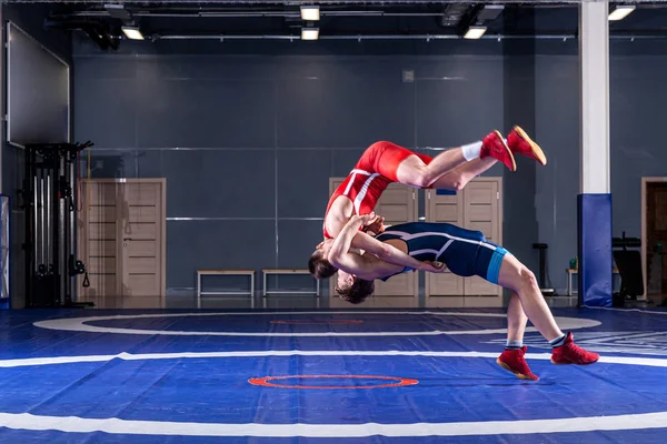 The concept of fair wrestling. Two greco-roman  wrestlers in red and blue uniform wrestling   on a wrestling carpet in the gym.The concept of fair wrestling