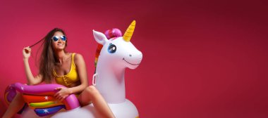 Yaz moda güzel kadın yaz giysileri eğlenmek, gülümseme ve balon ile poz üzerinde Unicorn float izole pembe arka plan