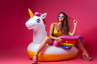 Yaz moda güzel kadın yaz giysileri eğlenmek, gülümseme ve balon ile poz üzerinde Unicorn float izole pembe arka plan