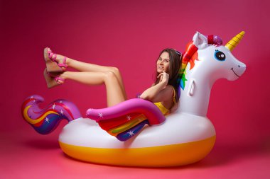 Yaz moda güzel kadın yaz giysileri eğlenmek, gülümseme ve balon ile poz üzerinde Unicorn float izole pembe arka plan