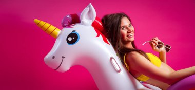 Yaz moda güzel kadın yaz giysileri eğlenmek, gülümseme ve balon ile poz üzerinde Unicorn float izole pembe arka plan
