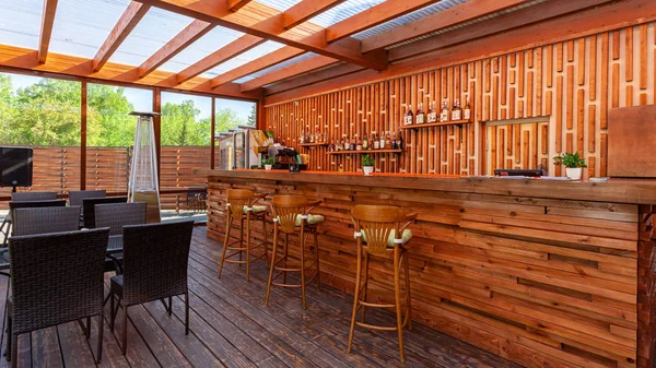 Summer empty outdoor cafe at park. Bar with modern design, wooden walls, high bar stools, wooden bar, tables