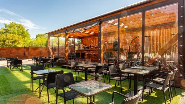 Summer empty outdoor cafe at park. Bar with modern design, wooden walls, high bar stools, wooden bar, tables
