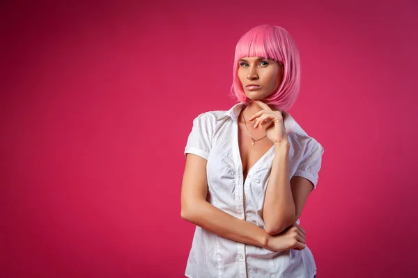 Concept of merry summer mood, relaxation and beauty. Close-up of a beautiful woman in a pink wig  in short attractive jeans, white shirt   posing on a pink background