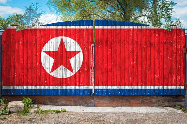 Close-up of the national flag of North Korea on a wooden gate at the entrance to the closed territory on a summer day. The concept of storage of goods, entry to a closed area, tourism in North Korea