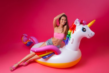 Yaz moda kız, pembe ve neşeli ruh hali. Bir mayo güzel ince kadın oturuyor, eğlenceli ve pembe izole arka planda beyaz şişme Unicorn yaşam zevk
