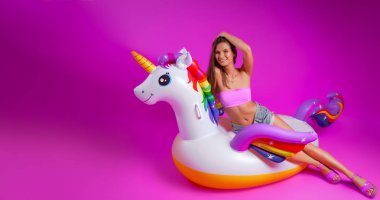 Yaz moda kız, pembe ve neşeli ruh hali. Bir mayo güzel ince kadın oturuyor, eğlenceli ve pembe izole arka planda beyaz şişme Unicorn yaşam zevk