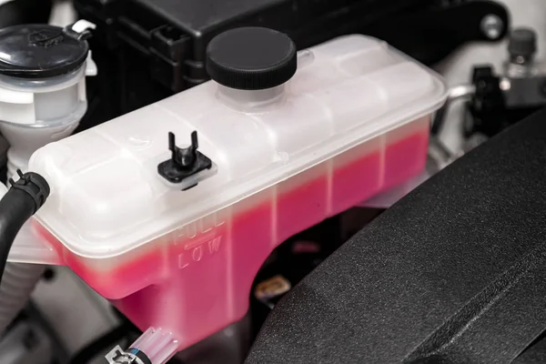 Close-up white expansion tank with pink antifreeze. Car coolant level in radiator system in car, automotive part.