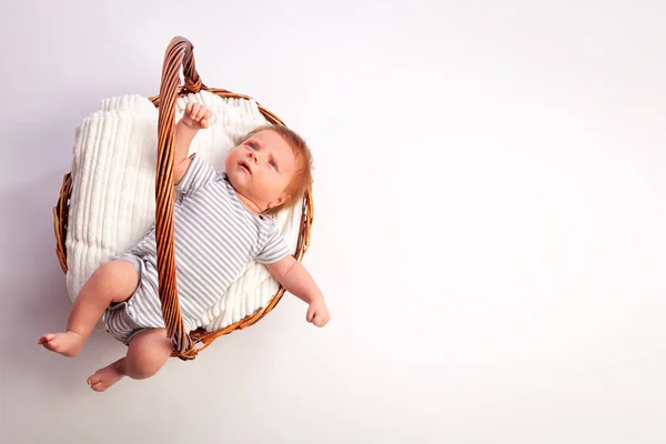 一个刚出生的男婴 1个月大 身着条纹连体衣 红头发 蓝眼睛在白色隔离背景的柳条篮子里的白色床上用品上 儿童概念 — 图库照片