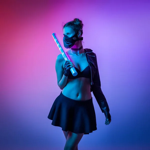 Concept on cosmic cosplay. ontemporary portrait a young athletic woman in black skirt, underwear, leather jacket  and highboots is holding a lightsaber and posing on neon blue-pink background