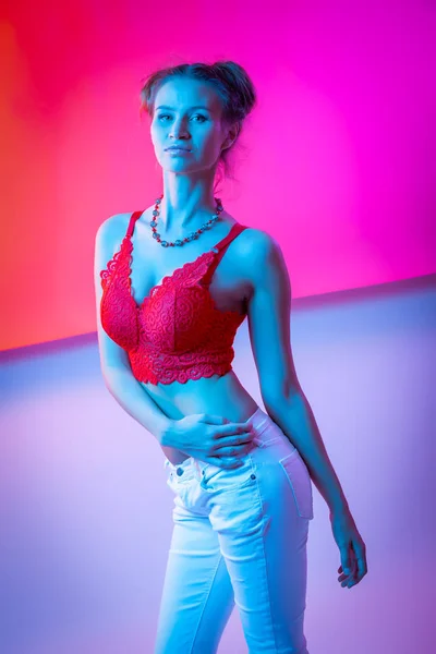 Cinematic night portrait of woman in  neon. High Fashion model girl in colorful bright neon lights posing in studio, portrait of beautiful woman in lingerie and jeans