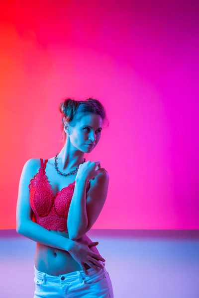 Cinematic night portrait of woman in  neon. High Fashion model girl in colorful bright neon lights posing in studio, portrait of beautiful woman in lingerie and jeans