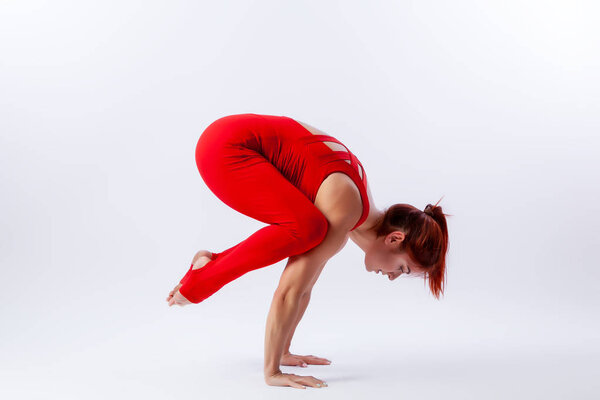 Beautiful slim woman in sports overalls  doing yoga, standing in an asana pose - cock on white  isolated background. The concept of sports and meditation. Training for stretching and yoga