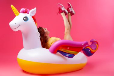 Yaz moda güzel kadın yaz giysileri eğlenmek, gülümseme ve balon ile poz üzerinde Unicorn float izole pembe arka plan