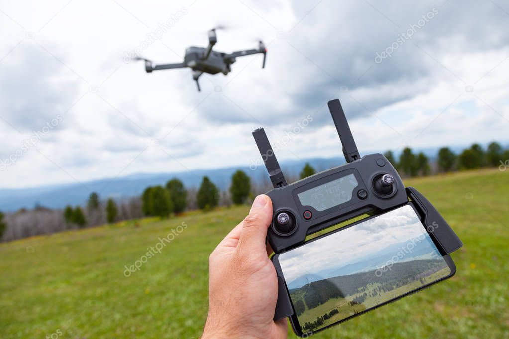 Landscaping on a quadrocopter. A young man holds in his hand a quadrocopter control panel with a monitor and an image of mountains; in the background is a quadrocopter