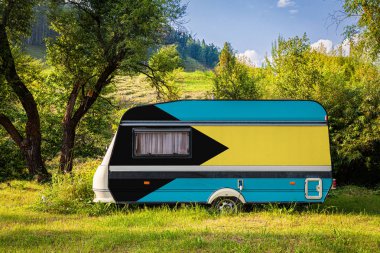 Bir araba römork, bir motor ev, Bahamalar ulusal bayrağı boyalı bir dağlık park halinde duruyor. Ülkeler arasında karayolu taşımacılığı, ticareti, ihracatı ve ithalatı kavramı. Arabayla seyahat