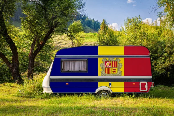 A car trailer, a motor home, painted in the national flag of Andorra stands parked in a mountainous. The concept of road transport, trade, export and import between countries. Travel by car