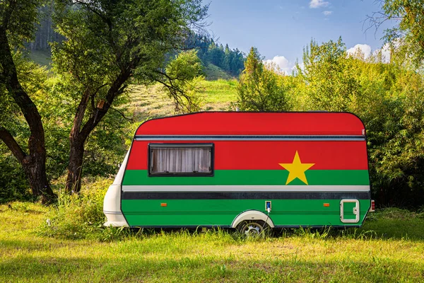 A car trailer, a motor home, painted in the national flag of Burkina Faso stands parked in a mountainous. The concept of road transport, trade, export and import between countries. Travel by car