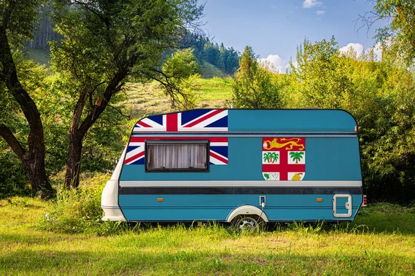A car trailer, a motor home, painted in the national flag of Fiji stands parked in a mountainous. The concept of road transport, trade, export and import between countries. Travel by car