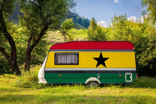 A car trailer, a motor home, painted in the national flag of Ghana stands parked in a mountainous. The concept of road transport, trade, export and import between countries. Travel by car