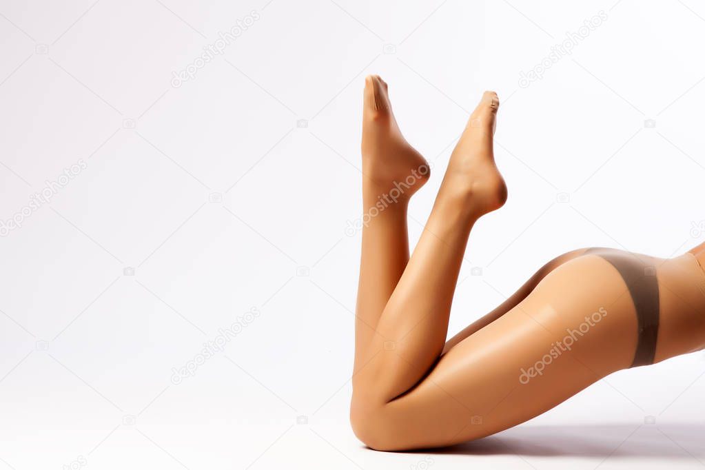 Close-up of beautiful woman's slim legs in flesh-colored nylon pantyhose posing in an elegant pose on a white isolated background. Concept of a woman's beauty, legs. Woman in hosiery.