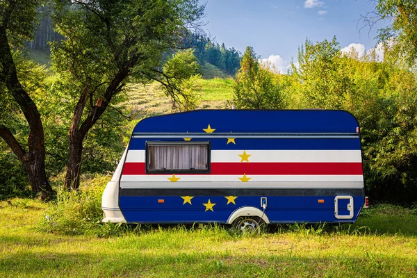 A car trailer, a motor home, painted in the national flag of Cape Verde stands parked in a mountainous. The concept of road transport, trade, export and import between countries. Travel by car