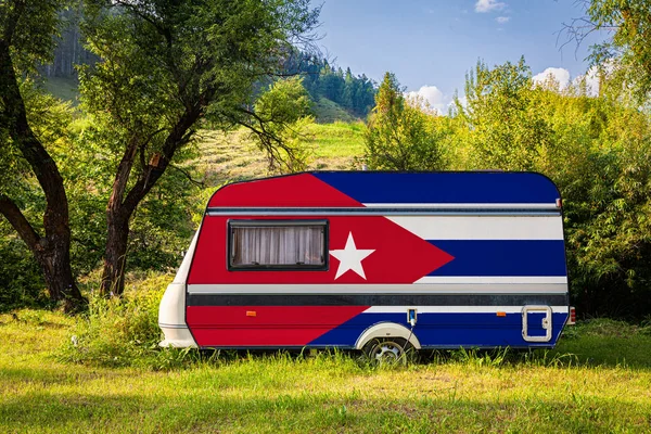 A car trailer, a motor home, painted in the national flag of Cuba stands parked in a mountainous. The concept of road transport, trade, export and import between countries. Travel by car