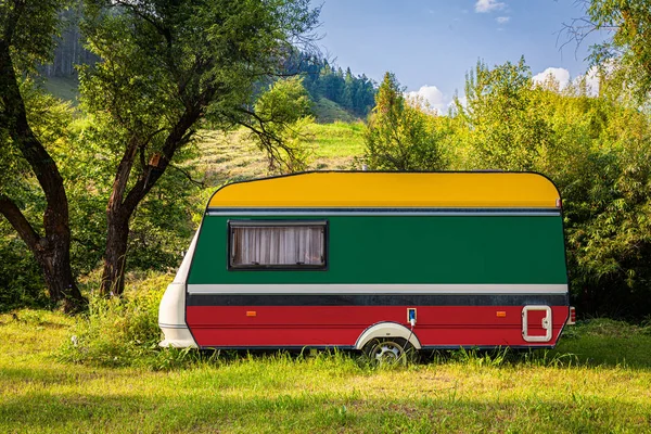 A car trailer, a motor home, painted in the national flag of Lithuania stands parked in a mountainous. The concept of road transport, trade, export and import between countries. Travel by car
