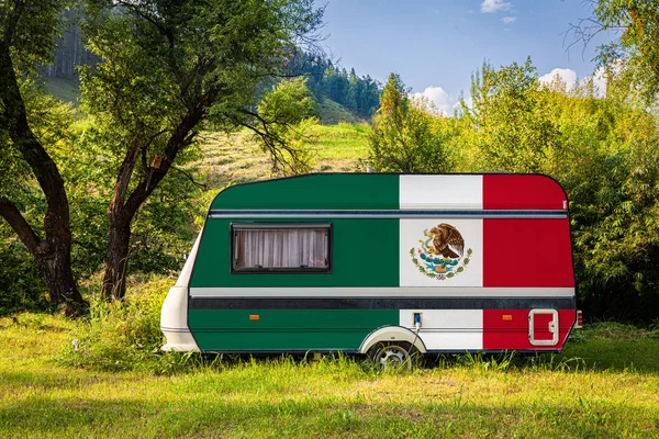 A car trailer, a motor home, painted in the national flag of Mexico stands parked in a mountainous. The concept of road transport, trade, export and import between countries. Travel by car