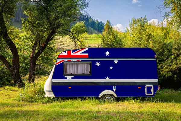 A car trailer, a motor home, painted in the national flag of  Australia stands parked in a mountainous. The concept of road transport, trade, export and import between countries. Travel by car