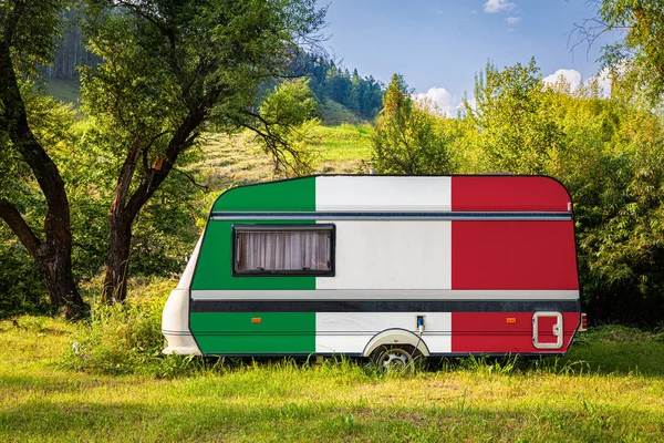 A car trailer, a motor home, painted in the national flag of Italy stands parked in a mountainous. The concept of road transport, trade, export and import between countries. Travel by car