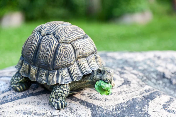 Close-up of a large turtle in a stone shell - decorations for the garden on a garden stone on a green grass background on a warm summer day
