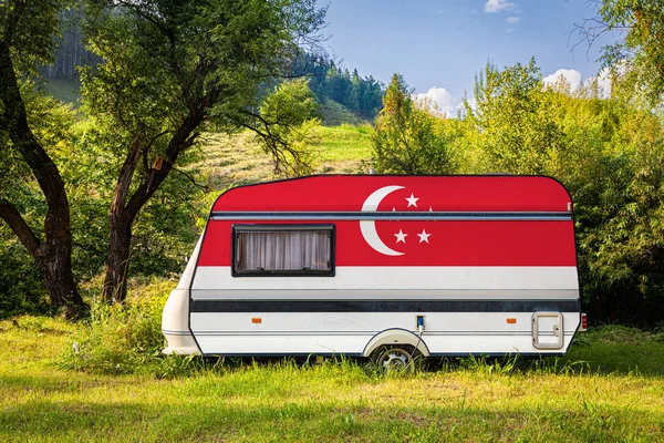 A car trailer, a motor home, painted in the national flag of  Singapore stands parked in a mountainous. The concept of road transport, trade, export and import between countries. Travel by car