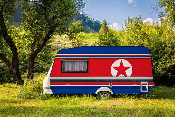 A car trailer, a motor home, painted in the national flag of  North Korea stands parked in a mountainous. The concept of road transport, trade, export and import between countries. Travel by car