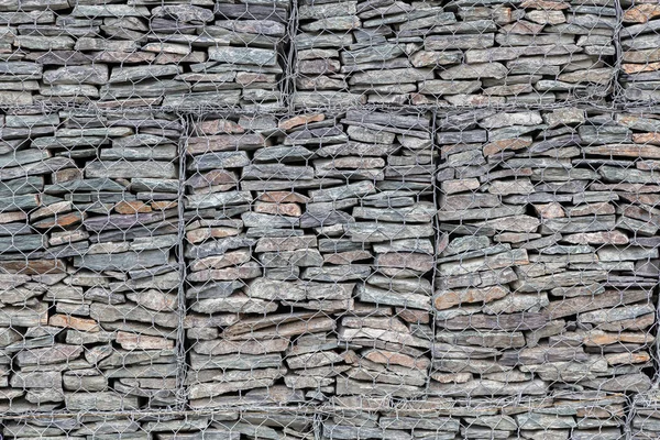 A wall lined with small gray stones behind a metal grate so that the mountains do not crumble. Stone texture