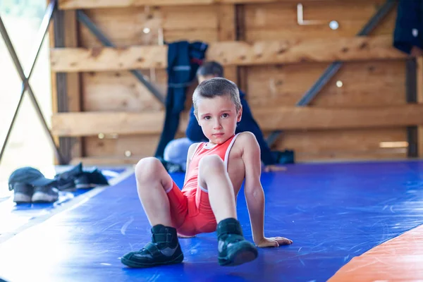 アルタイ ロシア2019年8月16日 赤いレスリングタイツの小さな男の子は スポーツ運動を行い ジムの青いレスリングカーペットのスポーツキャンプで陽気に笑顔 オープントレーニングとサマースポーツキャンプ — ストック写真
