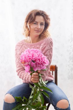 Narin kot pantolon ve örme kazak genç bir kadın pozlar ve elinde yatak odasında sabah şakayık güzel bir büyük buket tutar. Nazik bir arka plan üzerinde bir kızın romantik portre