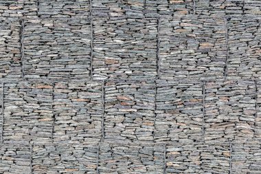 Dağların parçalanmaması için metal bir ızgaranın arkasında küçük gri taşlarla kaplı bir duvar. Taş doku