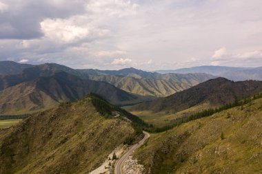 Dağlardan, yüksek dağlardan ve her iki tarafta sıcak bir yaz gününde yeşil bir ormandan geçen bir yol. Dağlardaki otoyol, hava manzarası.