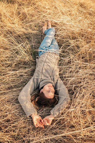 Posing woman in nature. Young woman in stylish clothes: knitted sweater and jeans posing  and  resting on field. Photos on vacation in the fall