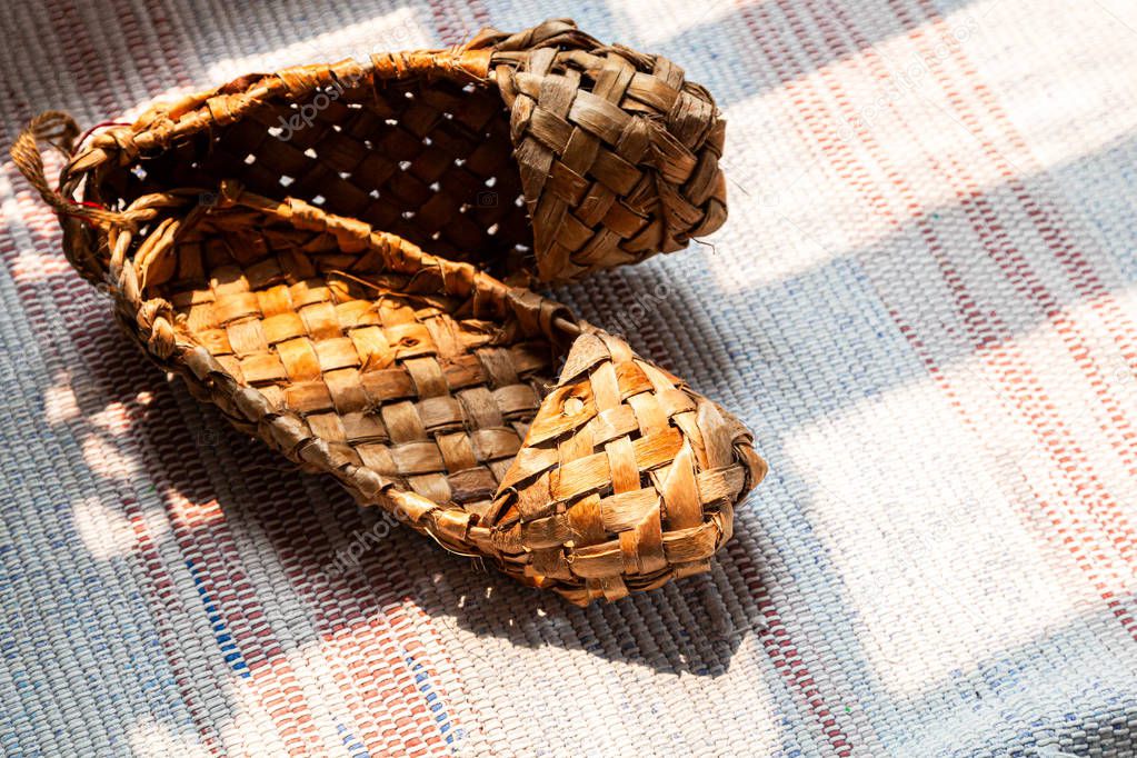 Old Russian sandals made of bark. Birch bark shoes, traditional old Russian shoes lie on an old traditional carpet in the sun.