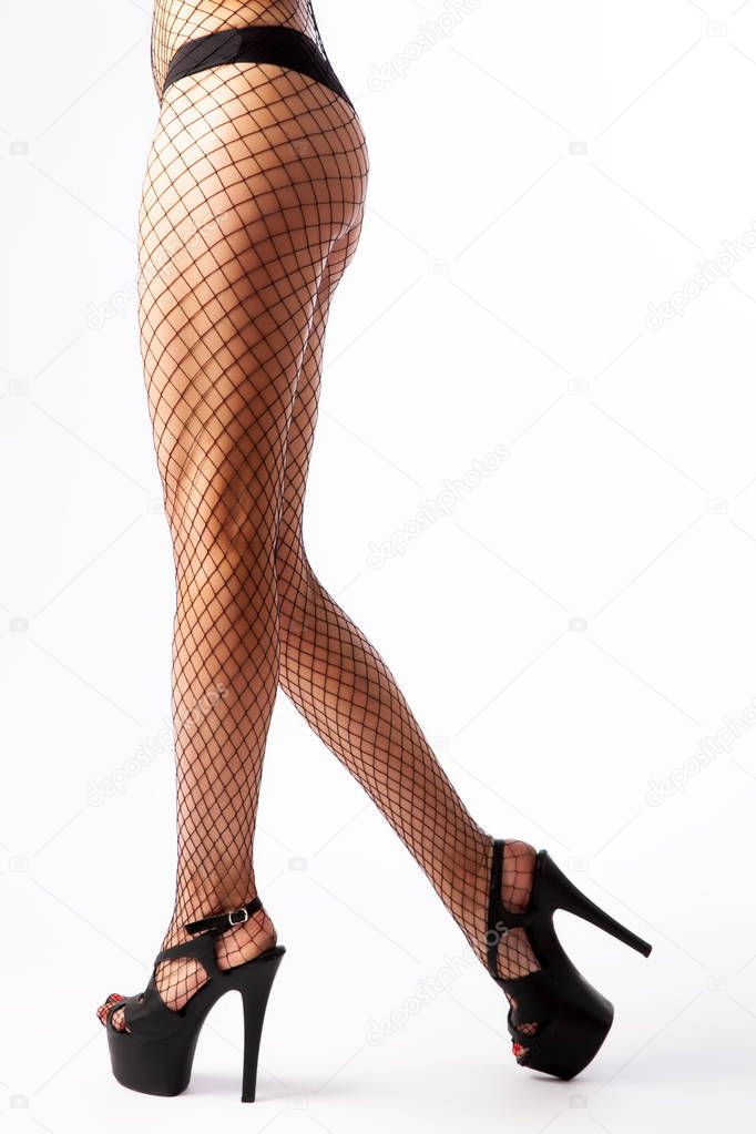 Legs of young caucasian woman in black mesh tights on high heels on white background. Fit and beautiful legs in sexy pantyhose. Woman in hosiery.